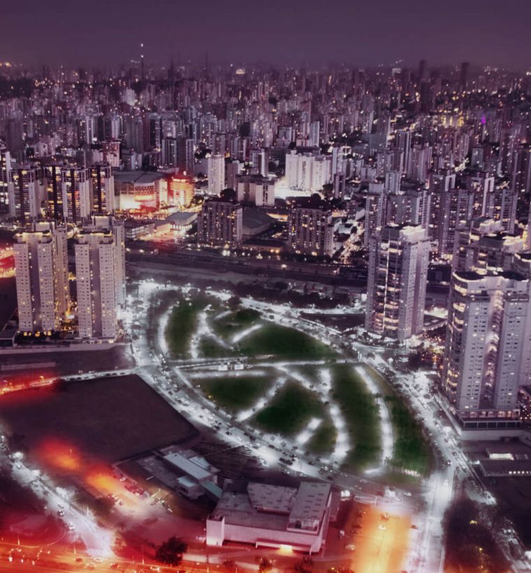 Vista aérea noturna do bairro, com o parque iluminado ao centro e a cidade ao redor