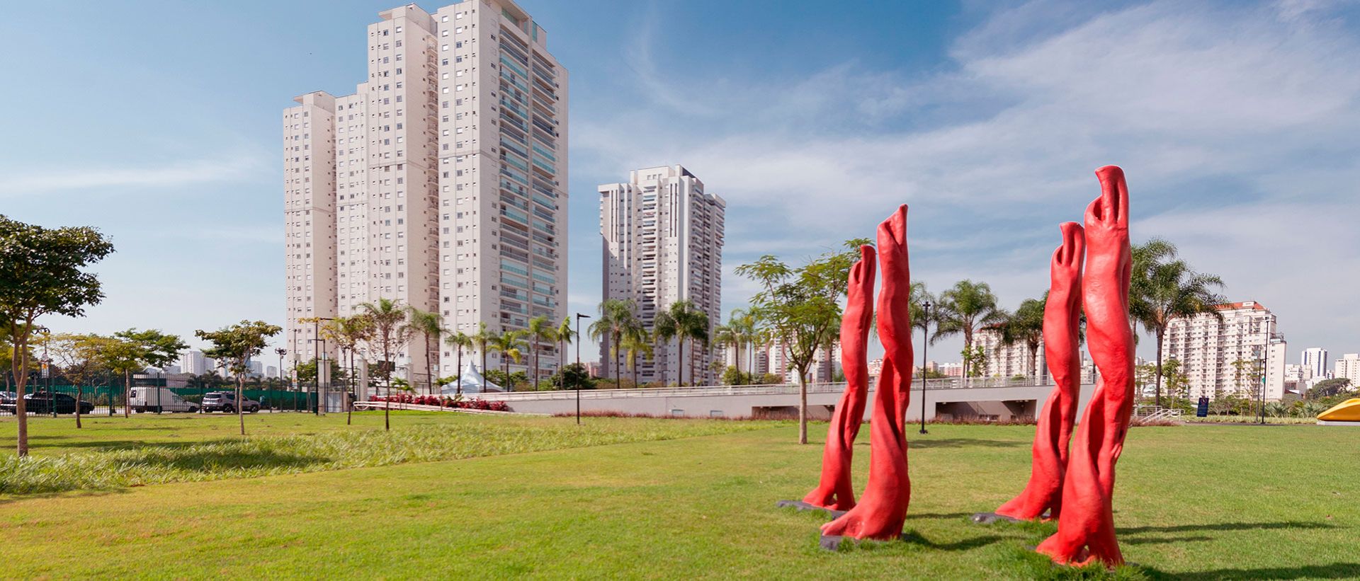 Gramado do parque com as esculturas vermelhas e as torres residenciais ao fundo