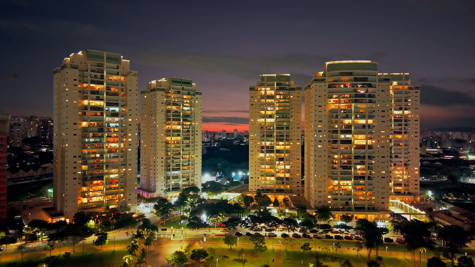 Vista aérea das torres residenciais do Jardim das Perdizes iluminadas ao entardecer, com o parque e a cidade ao redor